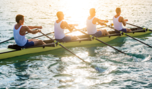 A group of people rowing a boat together in sync, representing teamwork showing why change management is important.