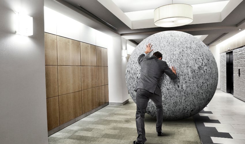 man pushing an immense ball in the office, metaphor for being overworked