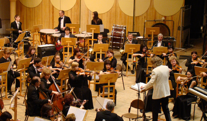 An orchestra in mid-performance, led by a conductor, symbolizing the coordinated effort required for successful project management.