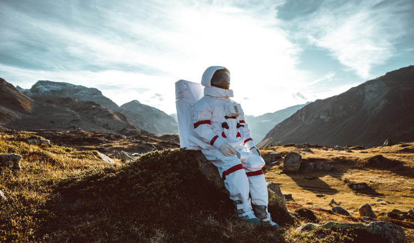 An astronaut seated on a rock in a mountainous landscape, representing exploration and pioneering strategies in project management.